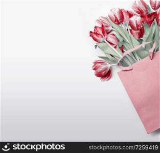 Red tulips in paper shopping bag on light gray background. Festive spring flowers bunch. Floral gift composing. Springtime holiday , greeting or sale concept. Copy space for your design
