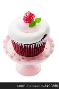 Red Velvet cupcake with pink and white whipped cream cheese icing, and a sugared raspberry with a sprig of mint as garnish. Served on a mini cupcake pedestal. Shot on white background.
