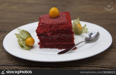Red Velvet, fresh delicious diet cake with berry Physalis at Dukan Diet on a porcelain plate with a spoon on a wooden background.