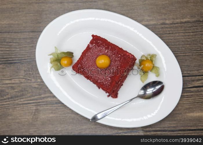 Red Velvet, fresh delicious diet cake with berry Physalis at Dukan Diet on a porcelain plate with a spoon on a wooden background.