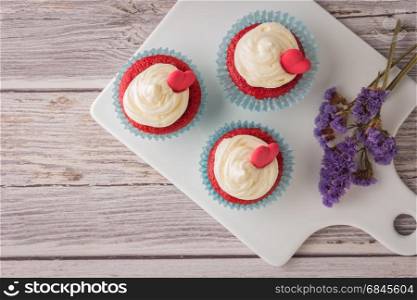 Red velvet heart cupcakes with cream cheese frosting and a red heart for Valentine's Day. Top view with copy space