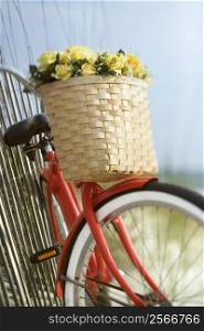 Red vintage bicycle with basket and flowers leaning against wooden fence at beach.