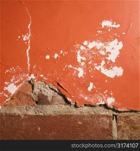 Red wall with cracking plaster and brick.
