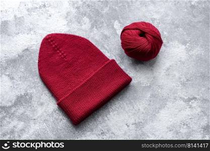 Red warm knitted women’s hat on a concrete background. Hobbies and leisure time. Red warm knitted women’s hat on a concrete background