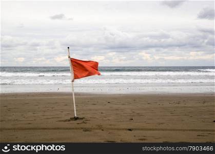 Red warning flag at the beach with waves and cloudy sky