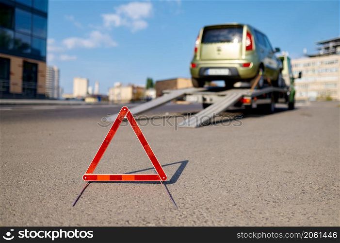 Red warning foldable triangle placed before tow track. Caution road sign and towing service. Closeup. Warning foldable triangle placed before tow track