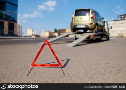 Red warning foldable triangle placed before tow track. Caution road sign and towing service. Closeup. Warning foldable triangle placed before tow track