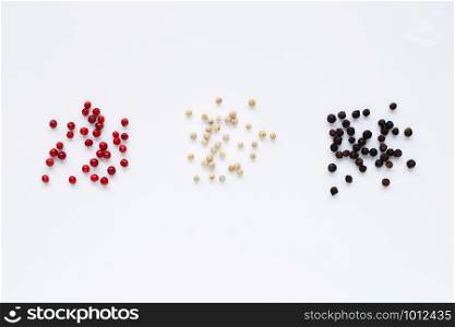 Red, white and black peppercorns on white background.