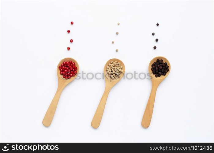 Red, white and black peppercorns with wooden spoon on white background.