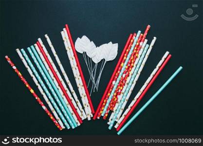 Red, white and blue paper straws and white leaves are scattered on a dark background.. Red, white and blue paper straws and white leaves are scattered on a dark background