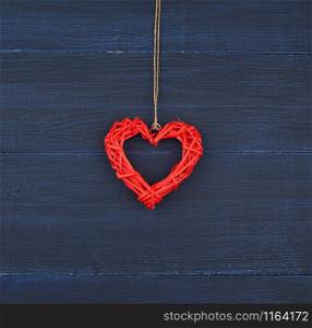 red wicker decorative heart hanging on brown rope, blue festive background for Valentine&rsquo;s day