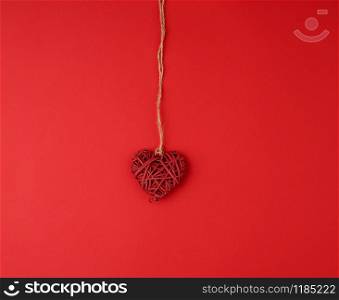 red wicker decorative heart hanging on brown rope, red festive background for Valentine&rsquo;s day