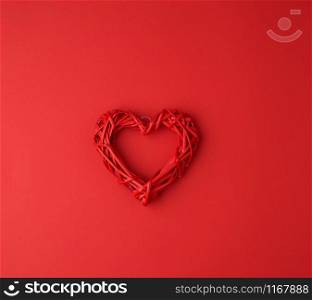 red wicker decorative heart on a red paper background, festive backdrop for Valentine&rsquo;s day