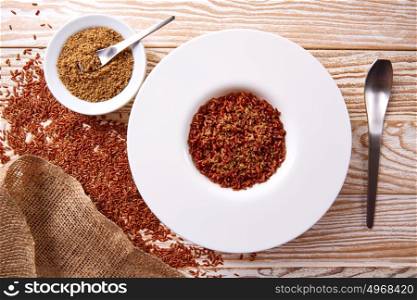 Red wild rice with sesame gomasio seasoning in a white plate over wooden board