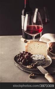 Red wine and cheese plate with fruits and nuts on concrete background