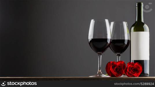 Red wine and roses. Two glasses of red wine and heart shaped roses on wooden table, gray copy space