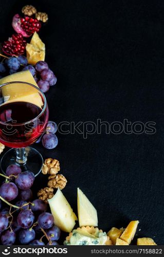 Red wine and snacks arranged in the form of a corner on a black background, with copy-space