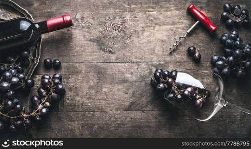 Red wine background with bottle and corkscrew , grapes and wine glass on dark vintage wooden, top view, frame