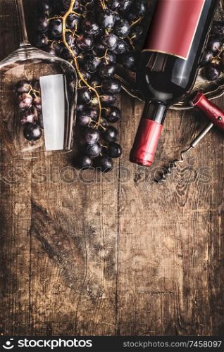Red wine bottle and glass with grapes on rustic wooden background. Top view. Border. Copy space. Wine tasting concept