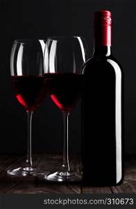 Red wine bottle and glasses on wooden table black background