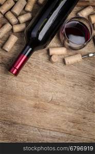 Red wine bottle, glass and corks on wooden table background