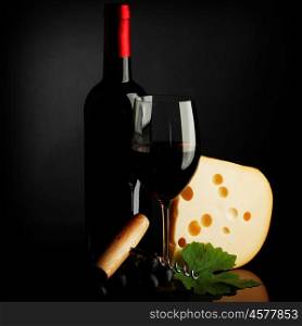 Red wine bottle, glass, cheese and corkscrew on dark background