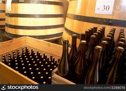 Red wine bottles with wine barrels in background, Italy.