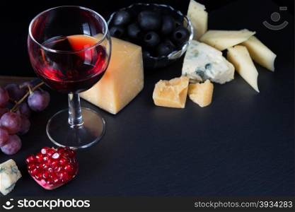 Red wine, cheese, pomegranate, black olives and grapes on a black background