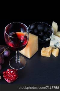 Red wine, cheese, pomegranate, black olives and grapes on a black background