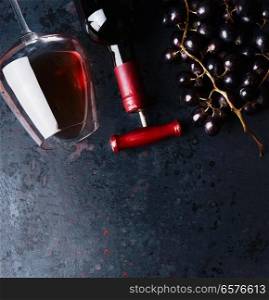 Red wine concept.  Glass with red wine,  bottle and red grape clusters on black rustic background, top view. Place for your design, text, article, advertisement or product.