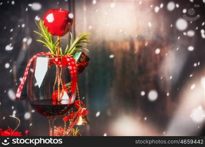 Red wine glass with Christmas decoration at dark wooden background with snow
