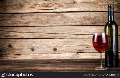Red wine in a glass and in a bottle on the table. On a wooden background.. Red wine in a glass and in a bottle on the table.