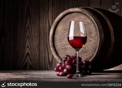 Red wine in glass and bunch of grapes on background of wooden barrels. Red wine in glass and bunch of grapes