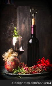 Red wine in goblet and bottle with festive Christmas decoration at dark wooden background, side view