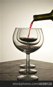 Red Wine pouring into a wineglass behind two other glasses - silhouette with warm tones