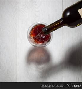 Red wine pouring into glass from bottle on white wooden table. Top view. Red wine pouring into glass from bottle