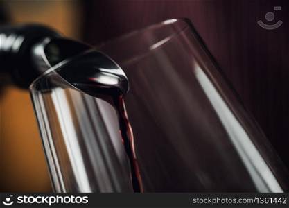 Red wine pouring into wine glass. Bottle with dropstop.