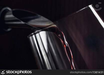 Red wine pouring into wine glass. Bottle with dropstop. Dark background.