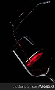 red wine pouring into wine glass isolated on black