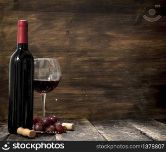 Red wine with a branch of grapes and a corkscrew. On a wooden background.. Red wine with a branch of grapes and a corkscrew.