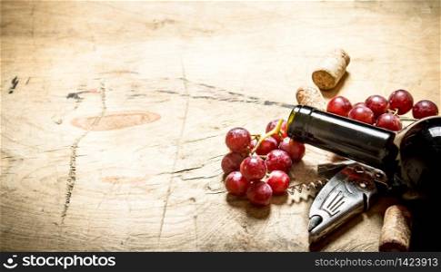 Red wine with a corkscrew, grapes and corks. On wooden background.. Red wine with a corkscrew, grapes and corks.
