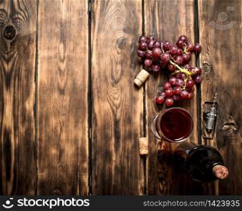 Red wine with a sprig of grapes and a corkscrew. On a wooden table.. Red wine with grapes