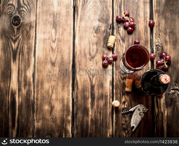 Red wine with a sprig of grapes and a corkscrew. On a wooden table.. Red wine with grapes