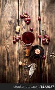 Red wine with a sprig of grapes and a corkscrew. On a wooden table.. Red wine with grapes