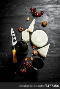 Red wine with fresh sheep cheese and grapes. On a black wooden background. Red wine with fresh sheep cheese and grapes.