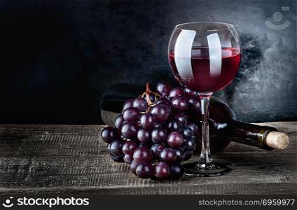 Red wine with grapes and bottle on a wooden table. The bottle lies. Dark background.. Wine with grapes and bottle. Wine with grapes and bottle