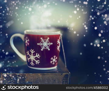 Red winter snowflakes cup with hot tea drink on rustic table with snow, side view