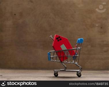 red wooden house in a metal miniature cart on a brown background. Real estate purchase concept, mortgage