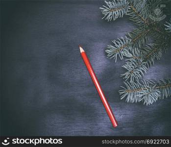 red wooden pencil and a green twig of a fir tree on a black background, empty space on the left