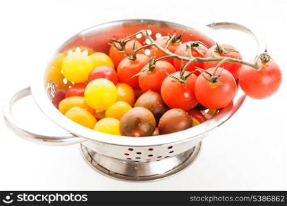 Red, yellow and black cherry tomatoes in colander on white